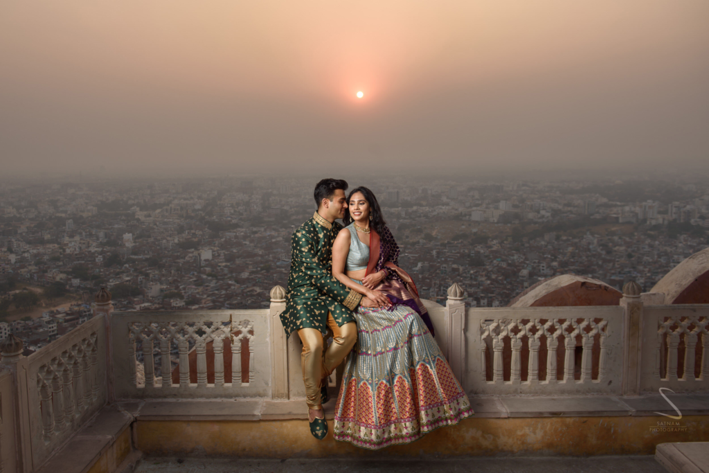 Pre-wedding couple sitting on a historic balcony with a breathtaking sunset city view.